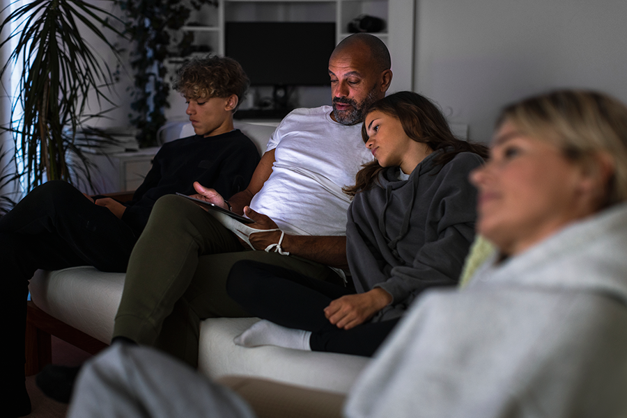 A family is sitting togther in a sofa looking at a tv or a tablet.